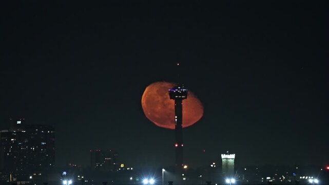 Vibrant Moon Rising Behind the Tower of Americas as Elevator Descends. San Antonio City Skyline Night Scene.