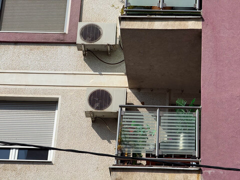 Building facade with air conditioners and balcony plants. Urban architecture, modern infrastructure, and residential environment in daylight.