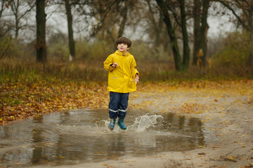 Happy child in a yellow raincoat jumping in puddles on a rainy autumn day in the park.