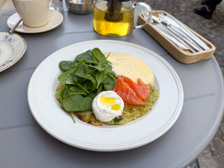 Plate with salmon, poached egg, spinach, and sauce in cafe. Healthy brunch, modern gastronomy, and nutritious meal in daylight setting.