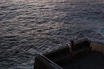 Woman holding phone on observation deck watching ocean