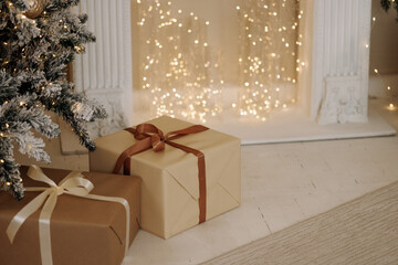 Two wrapped Christmas presents with ribbons under snowy tree near fireplace in cozy room with warm fairy lights and white wooden floor. Concept: holiday, winter, celebration, home decor.