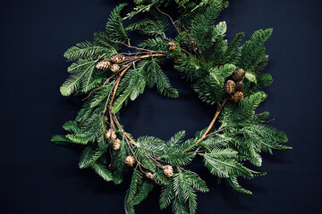 A minimalist holiday wreath made of evergreen branches, pinecones, and twigs on a dark background. Rustic elegance, natural textures, Scandinavian style, modern cabin trends