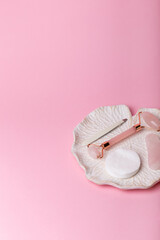 Stone roller facial massager, cotton pads, tweezers on pink background from above. Beauty rituals.