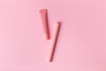 Mascara in pink bottle and lip gloss on pink background from above. Makeup tools