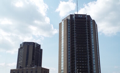 Two tall, dark-colored, hexagonal high-rise condominium towers with recessed balconies, set against...