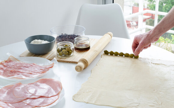 Mano colocando aceitunas sobre masa de pan. Preparaci&oacute;n artesanal de pan de jam&oacute;n. 