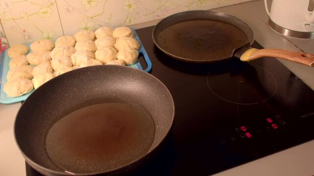 caucasian home cook places patties on stove and preheats pan, close-up of nonstick skillet and empty pan beside tray