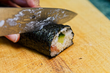 Hand Cutting Vegetable Maki Sushi Roll with Fresh Tuna on Cutting Board
