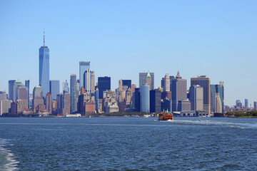 manhattan skyline and orange ferry boat navigating toward new york island