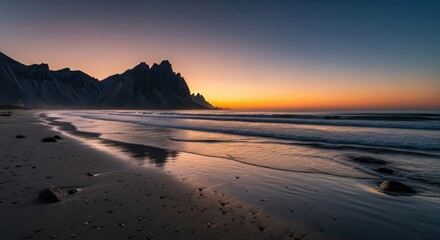 Dramatic coastal landscape at sunset with rugged mountains and serene ocean waves reflecting golden light