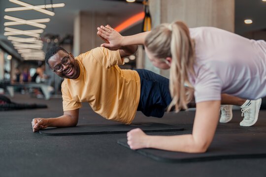 Diverse Fitness Partners In Colorful Athletic Wear Celebrate Together While Performing Side Planks At Modern Gym