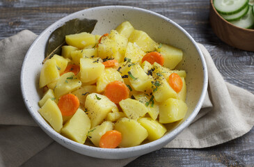 Homemade vegetable stew with potatoes, carrots, and herbs served in a rustic bowl with fresh cucumbers on wooden table. Warm, healthy comfort food with natural colors and soft light