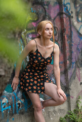 Blonde sensual woman with long legs posing confidently in front of a colorful graffiti wall, wearing a short floral dress. Urban fashion meets vibrant street art in this expressive portrait.