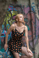 Blonde sensual woman with long legs posing confidently in front of a colorful graffiti wall, wearing a short floral dress. Urban fashion meets vibrant street art in this expressive portrait.