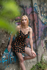 Blonde sensual woman with long legs posing confidently in front of a colorful graffiti wall, wearing a short floral dress. Urban fashion meets vibrant street art in this expressive portrait.