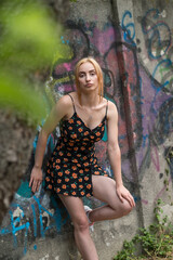 Blonde sensual woman with long legs posing confidently in front of a colorful graffiti wall, wearing a short floral dress. Urban fashion meets vibrant street art in this expressive portrait.