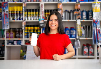 Young woman working in an auto parts store holding a smartphone with a blank white screen