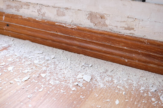 Close-up of a weathered wall with moisture damage and debris on the floor - Powered by Adobe