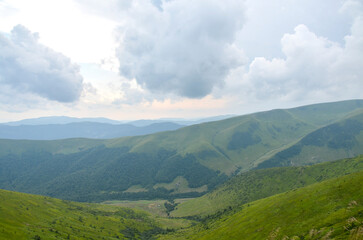 Rolling green hills extend into distant mountains beneath a dramatic, cloud-filled sky, creating a calm, expansive mood perfect for nature and outdoor adventure themes. Svydovets, Carpathians, Ukraine