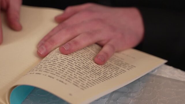 A close-up of hands on an open book with Hebrew text. This intimate shot conveys study, faith, and tradition. Perfect for projects on Judaism, religion, or learning.
