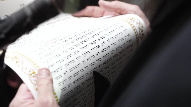 A man's hands hold a sacred scroll with Hebrew text. This intimate shot conveys faith, tradition, and study. Perfect for content on Judaism, scripture, and religious ceremonies.