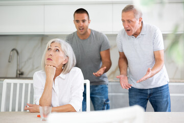 Fototapeta premium Adult woman sits at table and thinks how to resolve conflict with her husband and son