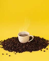 Cup of coffee on roasted coffee beans against yellow background. Minimal coffee concept.