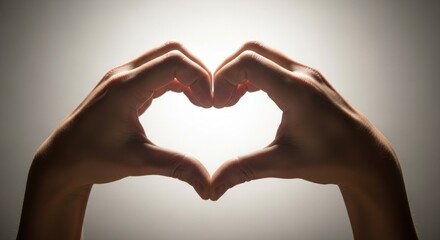 Obraz premium Silhouette of two hands forming a heart shape, brightly backlit on a gradient background