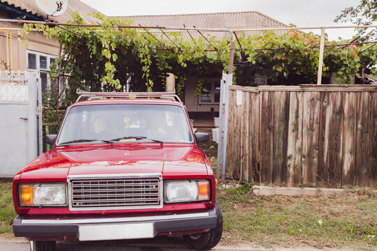 A senior Caucasian couple drives out of the yard in an old car.