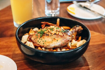 Traditional Quebec poutine with duck confit served in a black bowl at a restaurant
