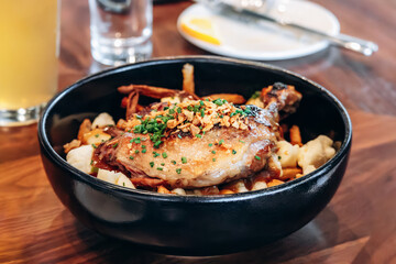 Traditional Quebec poutine with duck confit served in a black bowl at a restaurant