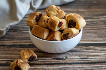 Pile of homemade roll cookies in pillow shape filled with jam in bowl on wooden russtic table