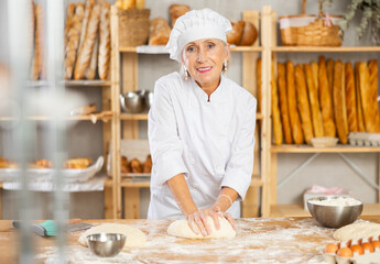 Baker senior woman kneads dough, creates dough from flour, yeast and water for making buns and croissants. Processing of creating croissants in bakery
