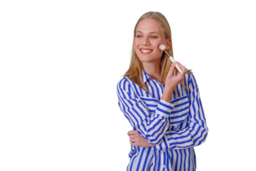 Woman smiling while applying blush to her cheek with a makeup brush, creating a beautiful look, transparent background