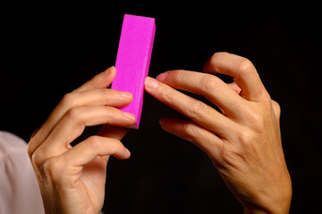 Woman using pink nail buffer to smooth and polish nails — manicure and hand care close-up