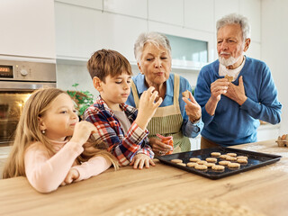 Portrait of grandparents and grandchildren having fun together preparing and eating baked dessert food in kitchen at home