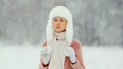 Young woman outdoors, girl in winter hat, sweater on snowy forest background with snowflakes