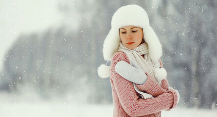 Young woman outdoors, girl in winter hat, sweater on snowy forest background with snowflakes