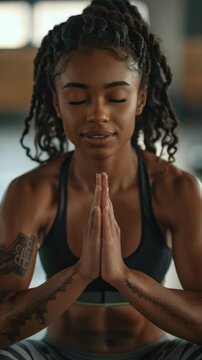 Young woman with a fit physique and tattoos practicing meditation while wearing workout attire. Indoors, gym setting.