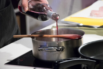 Pouring red wine into a saucepan while preparing sauce on a stovetop