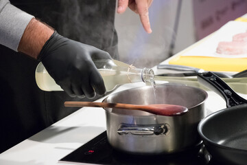 Pouring red wine into a saucepan while preparing sauce on a stovetop