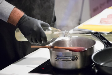 Pouring red wine into a saucepan while preparing sauce on a stovetop
