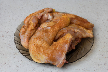 A top-down view of a dark brown glass plate stacked with a pile of raw chicken portions thighs, quarters generously seasoned with a red spice