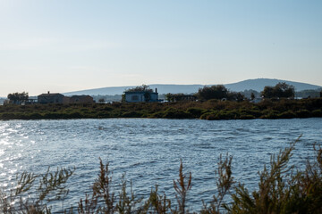 Fishermen huts along Chemin du Pilou in Villeneuve les Maguelone overlooking calm lagoon Mediterranean rural landscape with natural vegetation distant hills and authentic coastal atmosphere