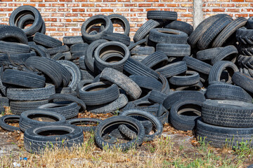 Close-up of a large pile of discarded and polluting tires in front of an old brick wall. Industrial...