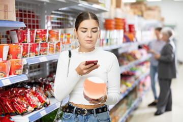 Young woman in supermarket scan QR code instant fast food. Girl buyer photo information on packaging of semi-finished product. Concept of affordable box-container feeding