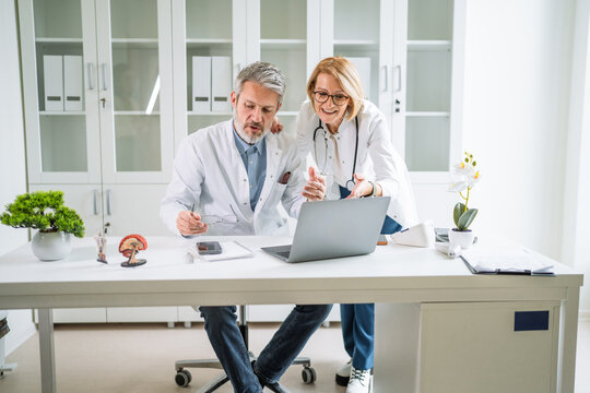 Doctors collaborating on laptop reviewing medical data in clinic