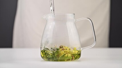 Dried flower tea petals being added to a glass teapot, followed by hot water pouring in to brew tea - Powered by Adobe