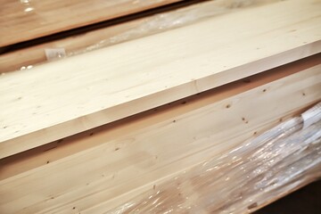 Planks of light-colored wood stacked neatly in a workshop, showcasing natural grain patterns and textures, ideal for construction and design projects